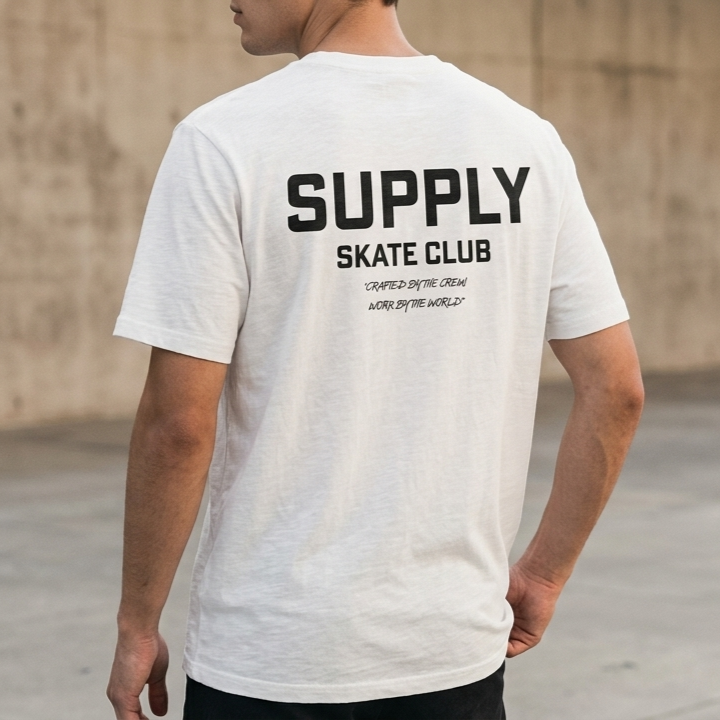 Person wearing a white t-shirt with 'SUPPLY SKATE CLUB' text on the back, standing against a concrete wall.